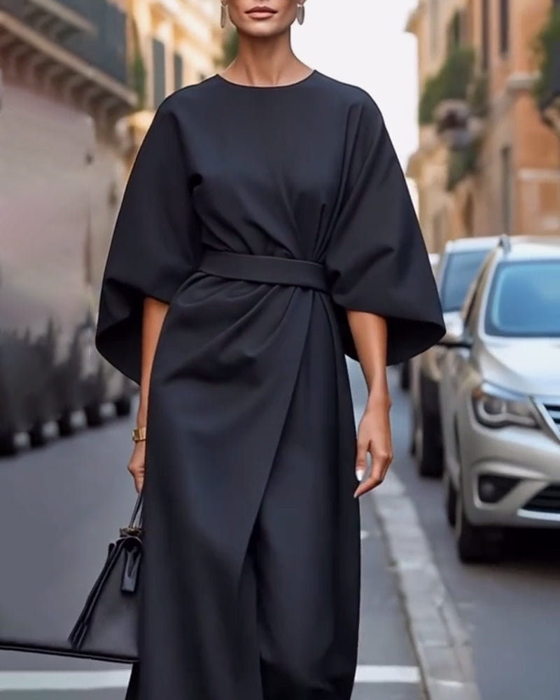 Black belted dress with wide batwing sleeves worn by a model with drop earrings, photographed close to the camera on a street. 4