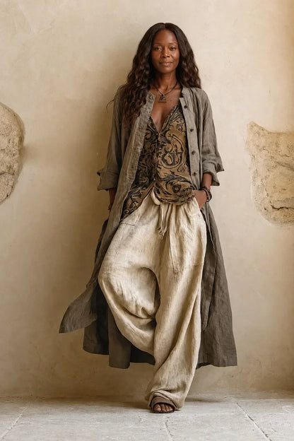 Model standing against a plaster wall in the full three-piece set: patterned top, loose cream trousers and a long grey-green cardigan worn open. 1