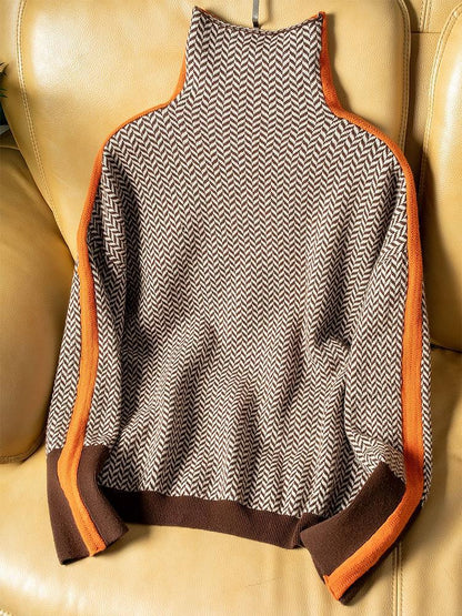 Flat lay of the brown and cream herringbone jumper on a tan leather chair, showing orange stripes and brown ribbed hem. 4