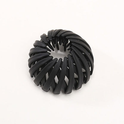 Single matte black spiral clip with overlapping curved slats and small inner teeth, photographed against a plain background. 14