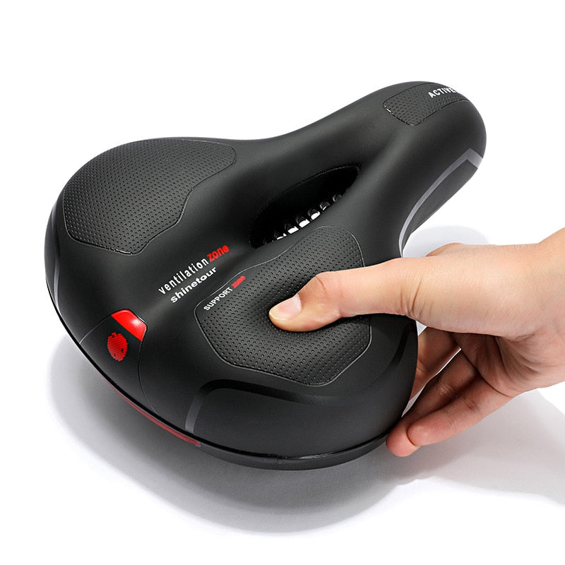 Hand pressing a thumb into the textured support pad of the black saddle, showing the soft padding and central cutout. 8