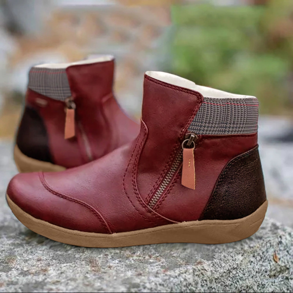 Pair of burgundy red leather ankle boots with side zip, checked collar and dark brown heel panel, shown on a rock. 5