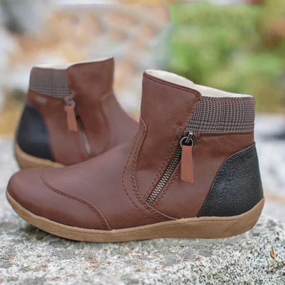 Pair of brown leather ankle boots with side zip, checked collar and contrasting black heel panel, shown on a rock outdoors. 3