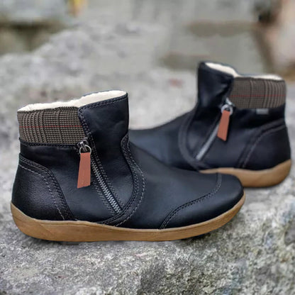 Pair of black leather ankle boots with side zip, orange-brown pull tab, checked collar and fleecy lining, on a stone surface. 2