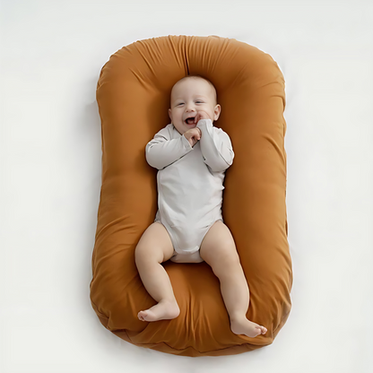 Overhead view of a smiling baby in a white bodysuit on a caramel-coloured cushion 3