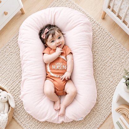 Smiling baby with a pink hair bow lying on a pale pink support pillow in a nursery 1