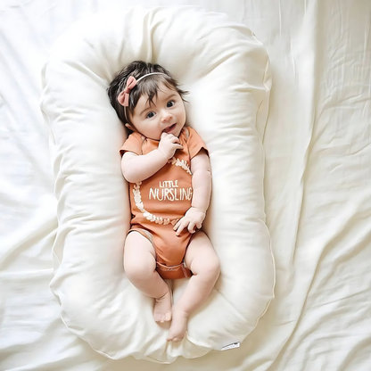 Overhead view of a baby in an orange bodysuit and bow headband on a cream cushion 5