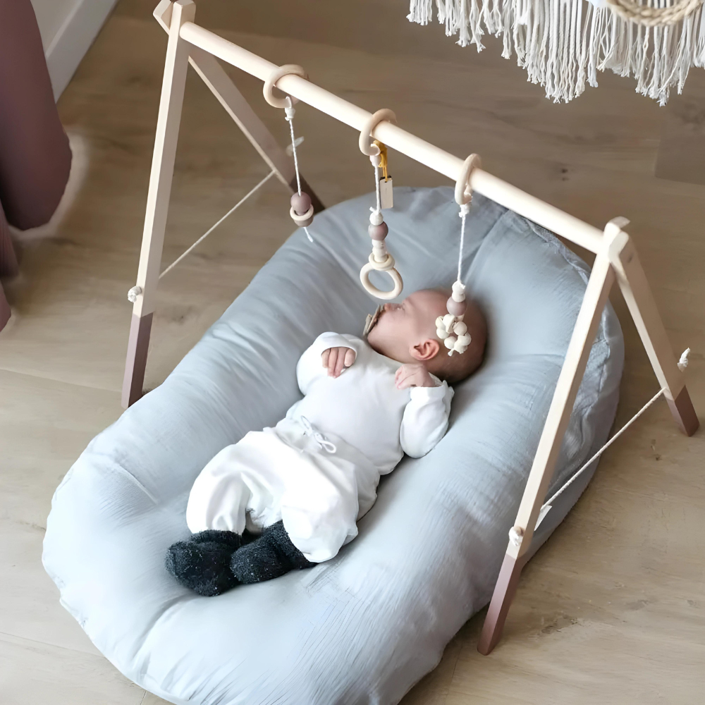 Baby lying on a pale blue cushion beneath a wooden play gym with hanging toys 6