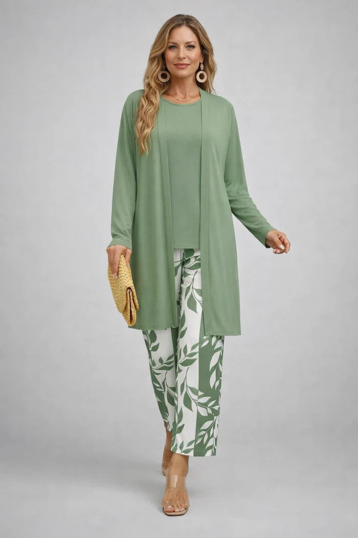 Model in a plain sage green long open cardigan and top with cream and green leaf-print trousers, carrying a straw clutch. 10