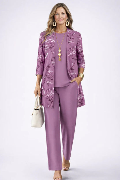 Model wearing the lilac set, the open cardigan printed with floral sprigs over a plain top and trousers, one hand in a pocket. 11