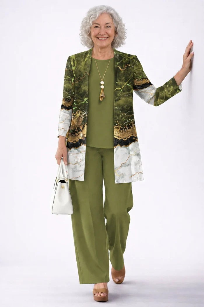 Older model leaning on a wall in the olive set, the open cardigan printed with a green and white marble design with gold veining. 19