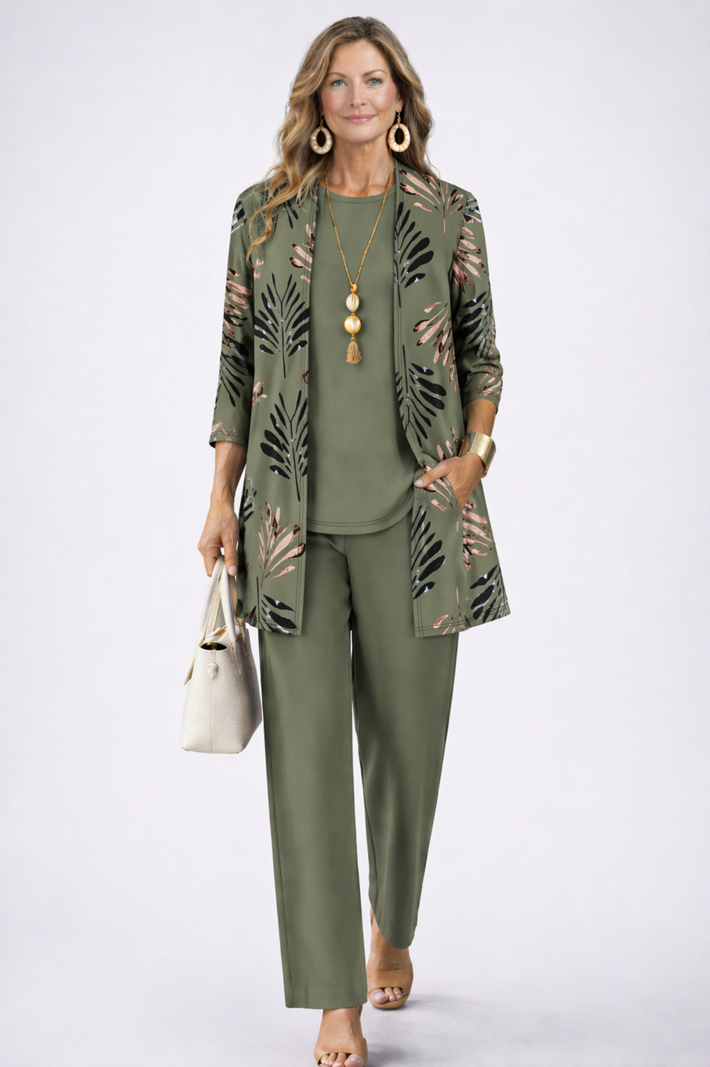 Model in the olive green set, the open cardigan printed with black and rose-gold palm leaves, one hand in a pocket. 2