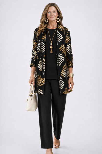 Model wearing the black set, the open cardigan printed with cream and gold palm leaves over a plain black top and trousers. 5