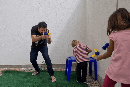 Man and a girl aim blue and yellow foam guns outdoors while a toddler stands between them 9
