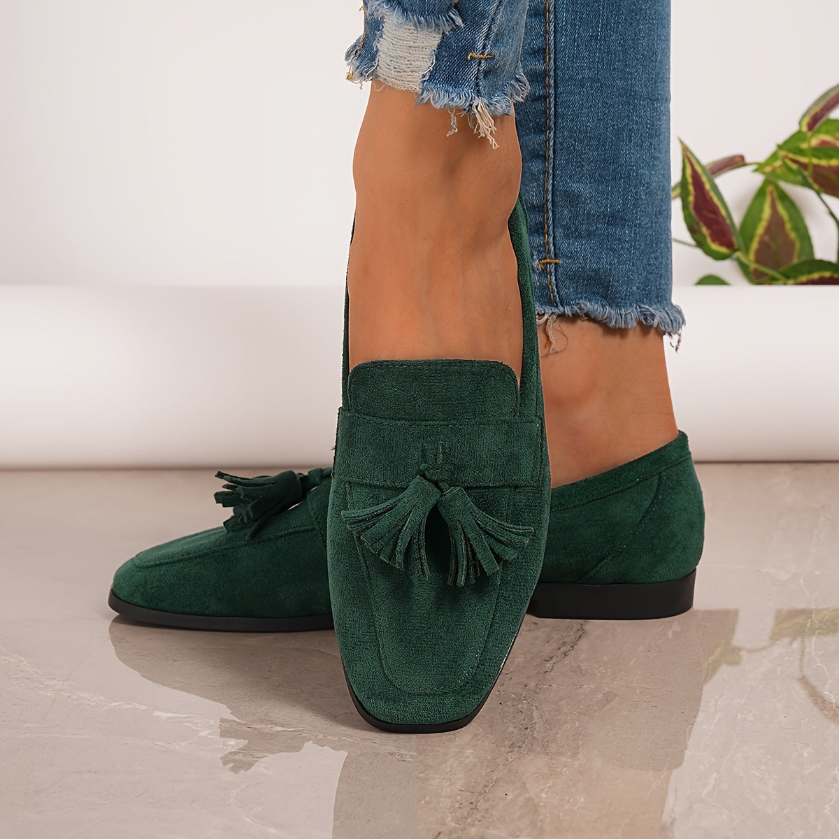 Black tasselled loafers worn on a grey marble floor with flowers in the background, front view 16
