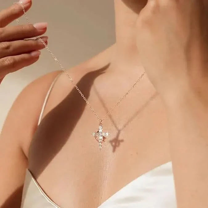 Woman in a white camisole holding up a fine chain with a sparkling crystal cross pendant, casting a shadow on her skin. 1