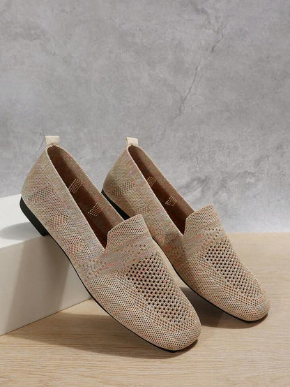 Pair of beige knit slip-on shoes with perforated toes resting against a white block, showing the interior. 7