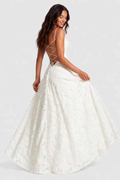 Back view of a white lace gown with criss-cross lace-up back, model holding the skirt out as she glances down. 8