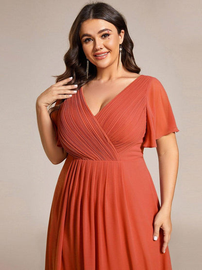 Close-up of the burnt orange pleated wrap V-neck bodice and flutter sleeves on a smiling plus-size model. 99