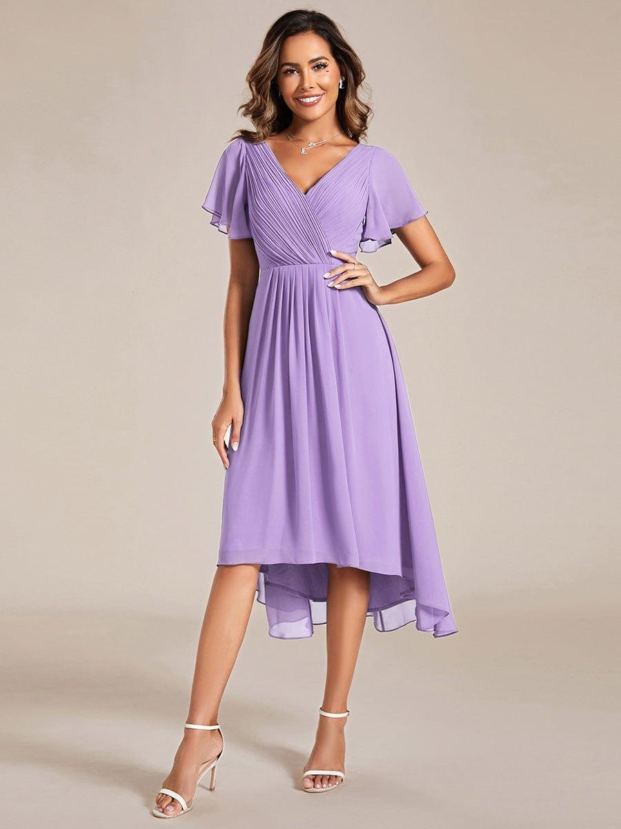 Model in a lilac chiffon dress with pleated wrap V-neck, flutter sleeves and high-low hem, one hand on her hip. 100