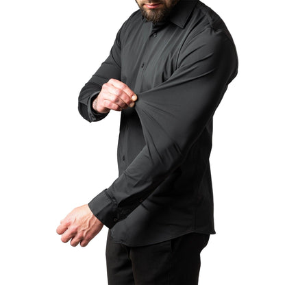Side view of a bearded model in a black long-sleeved shirt with black trousers, pinching and stretching the sleeve fabric. 1