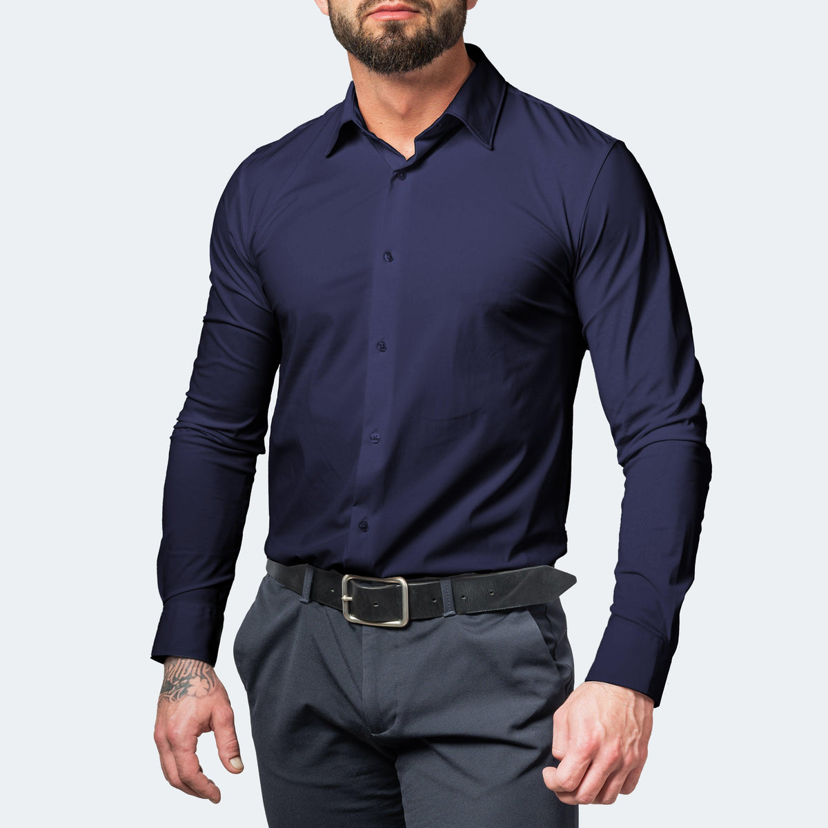Front view of a muscular, bearded model in a navy blue buttoned shirt, grey trousers and a black leather belt. 5