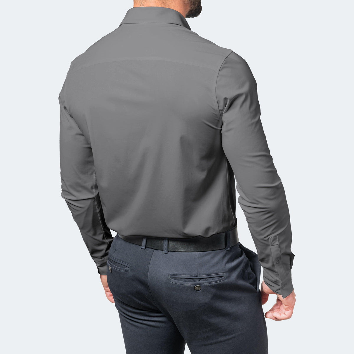 Back view of a model in a grey long-sleeved shirt tucked into navy trousers with a black belt, showing the smooth back panel. 6