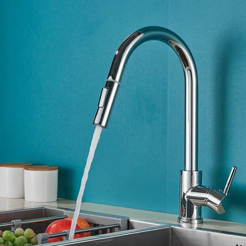 Polished chrome pull-out kitchen tap running water into a sink with fruit, against a teal tiled wall. 1