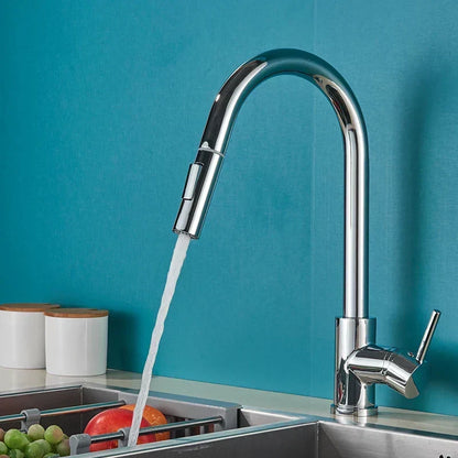Polished chrome pull-out kitchen tap running water into a sink with fruit, against a teal tiled wall. 1