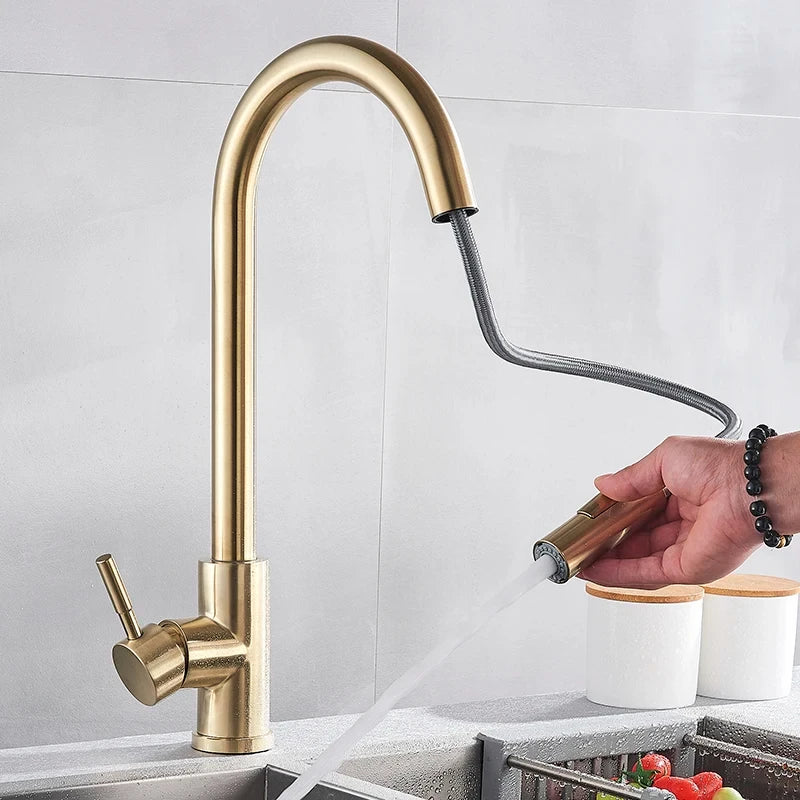 Brushed gold kitchen tap with the spray head pulled out on its flexible hose, held in one hand. 3