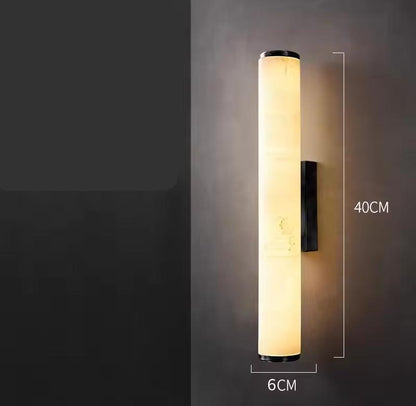 Shorter version of the lit cylindrical marble wall light on a grey wall, with dimension lines marking its height and width. 22