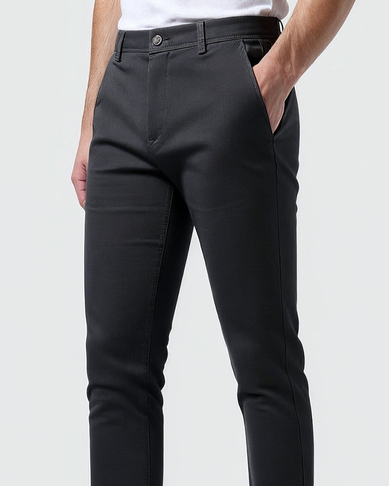 Close-up of charcoal chinos at the waist and hip, showing the button, belt loops and slanted side pocket with a hand inside. 10