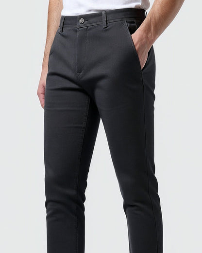 Close-up of charcoal chinos at the waist and hip, showing the button, belt loops and slanted side pocket with a hand inside. 10