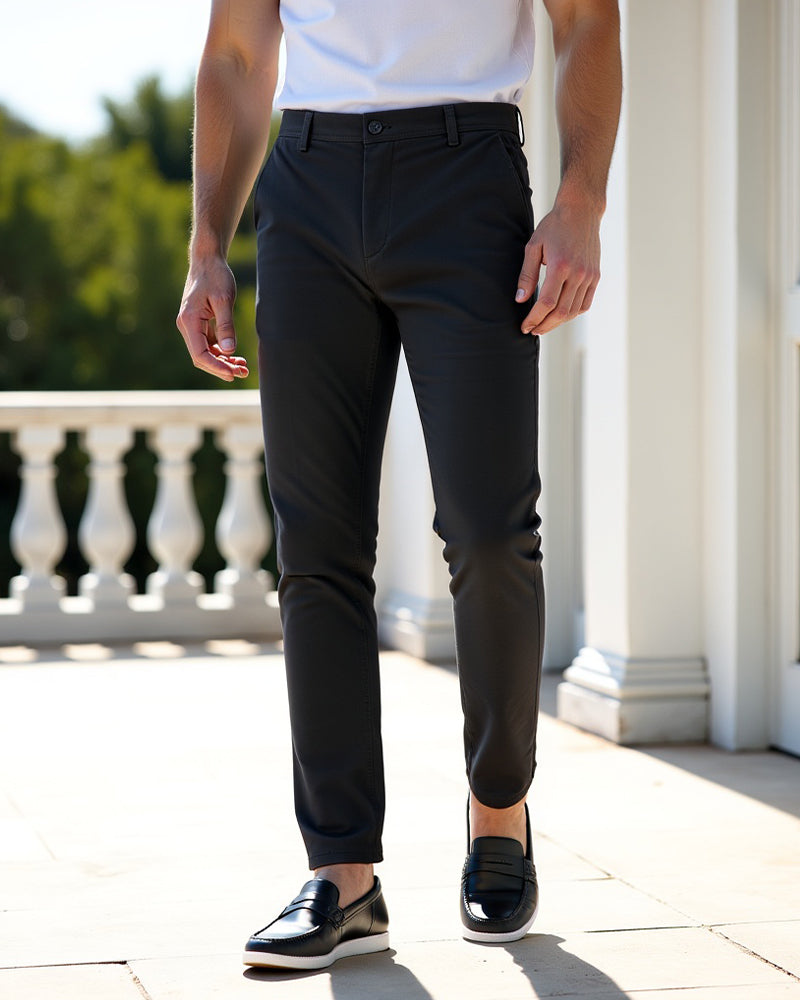 Charcoal chinos worn with a white t-shirt and black leather loafers on a sunlit terrace beside white pillars. 7