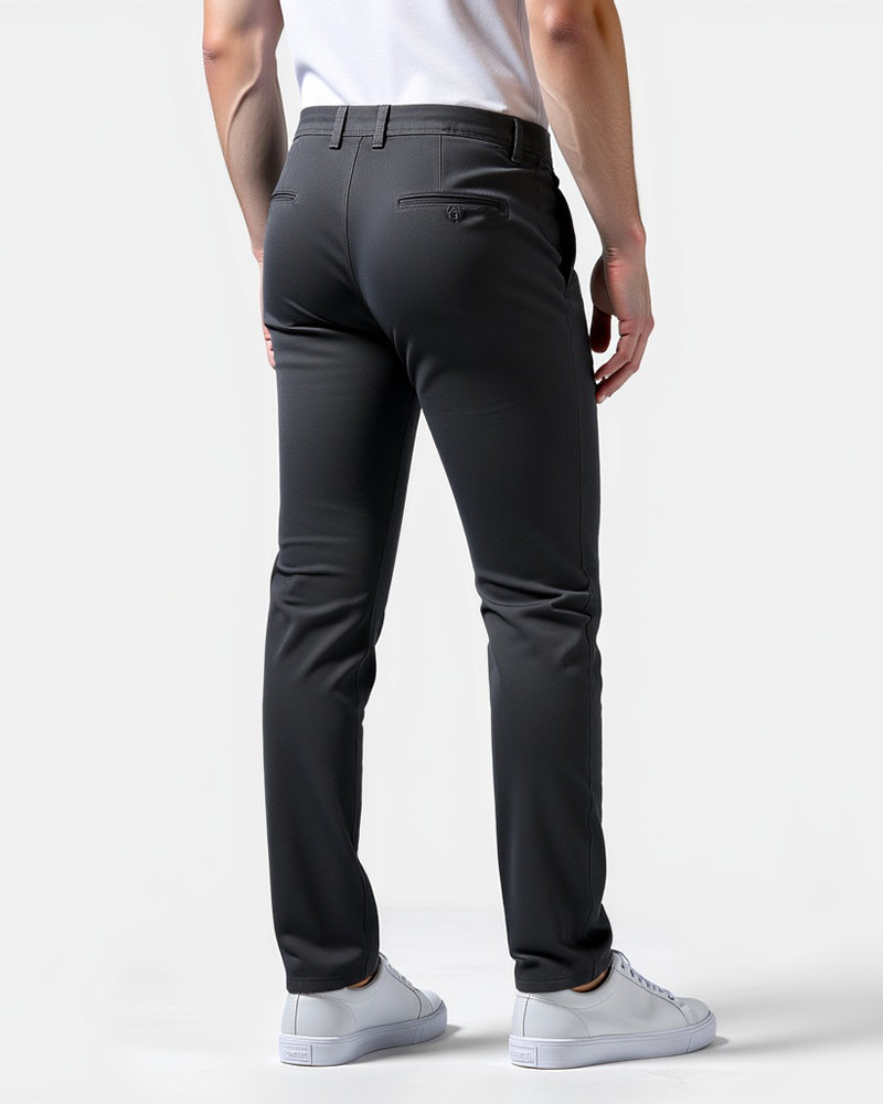 Back view of charcoal chinos on a model, showing a buttoned back pocket, belt loops and white trainers. 8