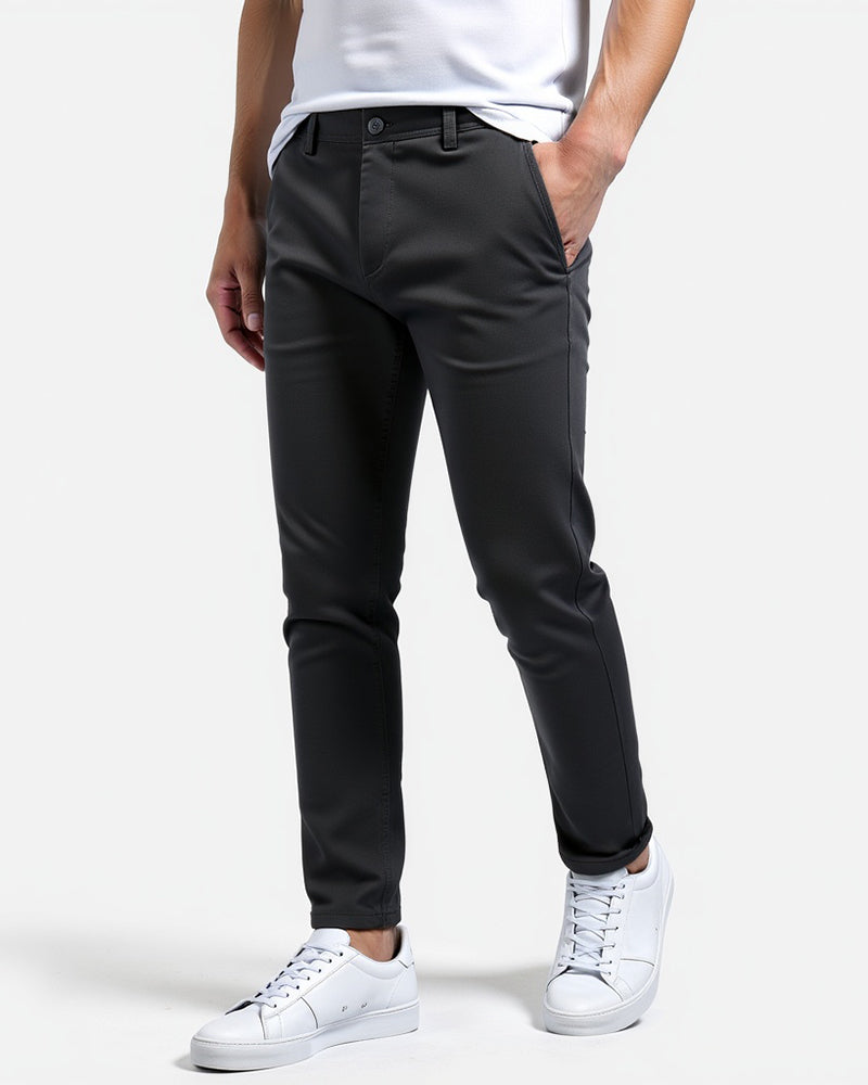 Charcoal slim chinos in a three-quarter view, worn with a white t-shirt and white trainers, one hand in the pocket. 12