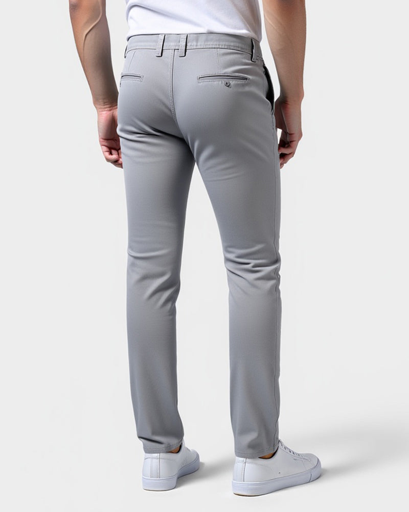Back view of light grey chinos on a model, showing two welted back pockets, belt loops and white trainers. 3