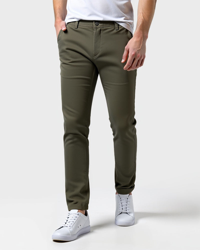 Olive green slim chinos worn with a white t-shirt and white trainers, one hand in a front pocket. 13
