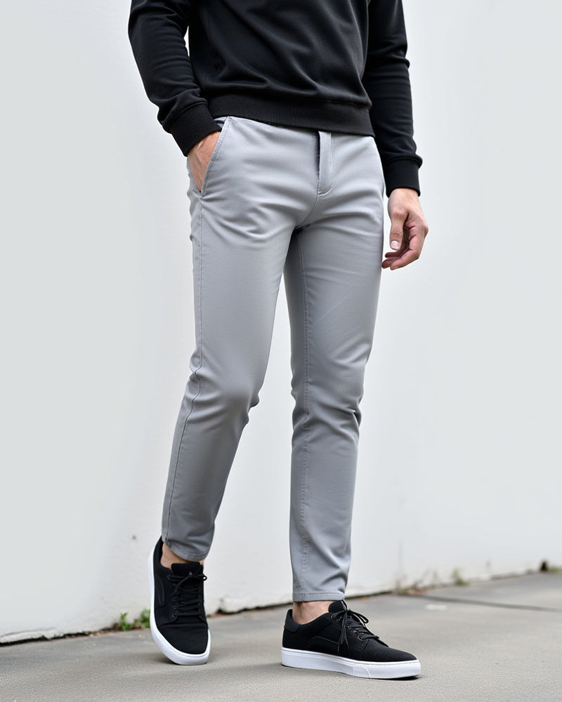 Light grey chinos worn with a black sweatshirt and black trainers, model standing in front of a white wall outdoors. 2