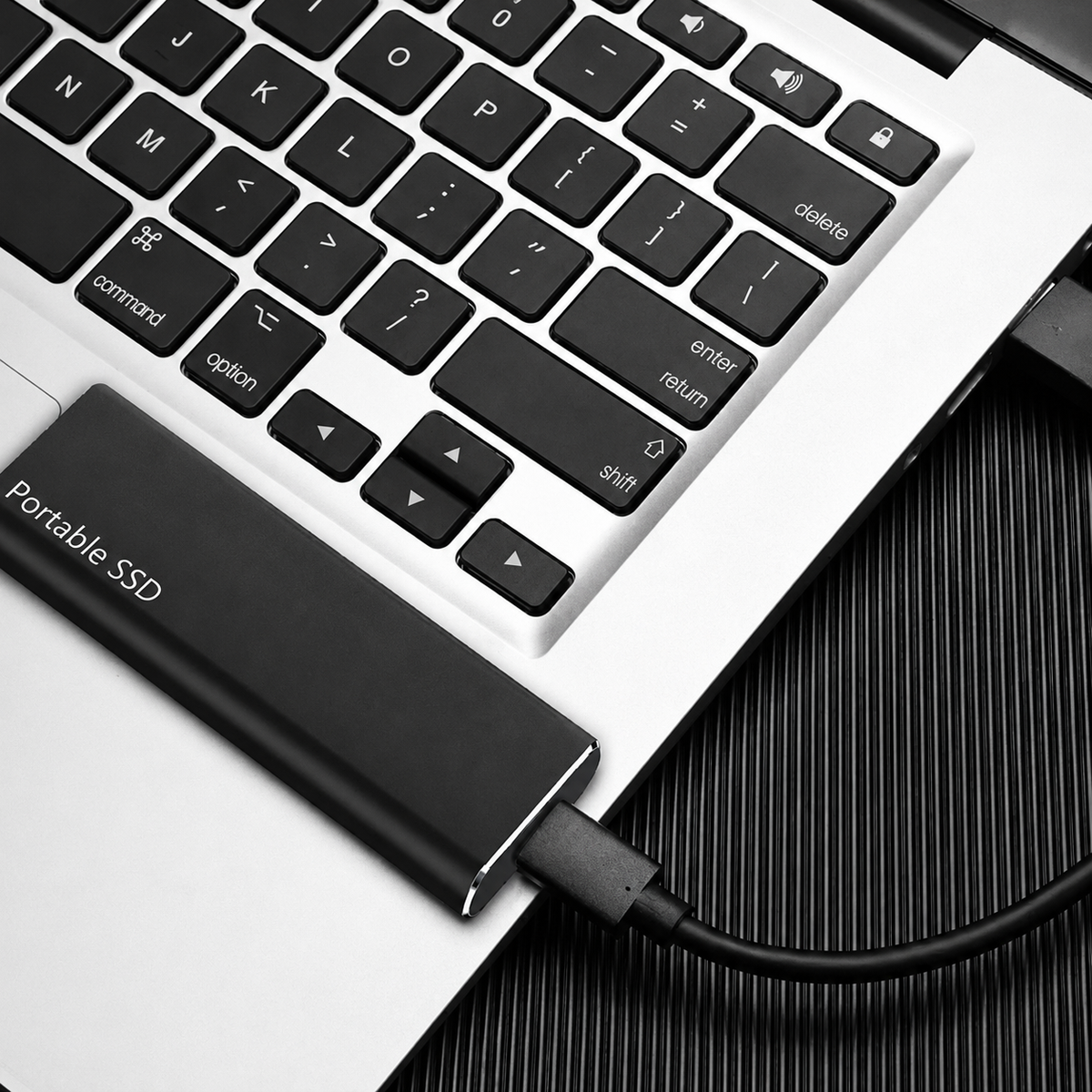 Black drive lying on a laptop palm rest with a black cable plugged into its end 8