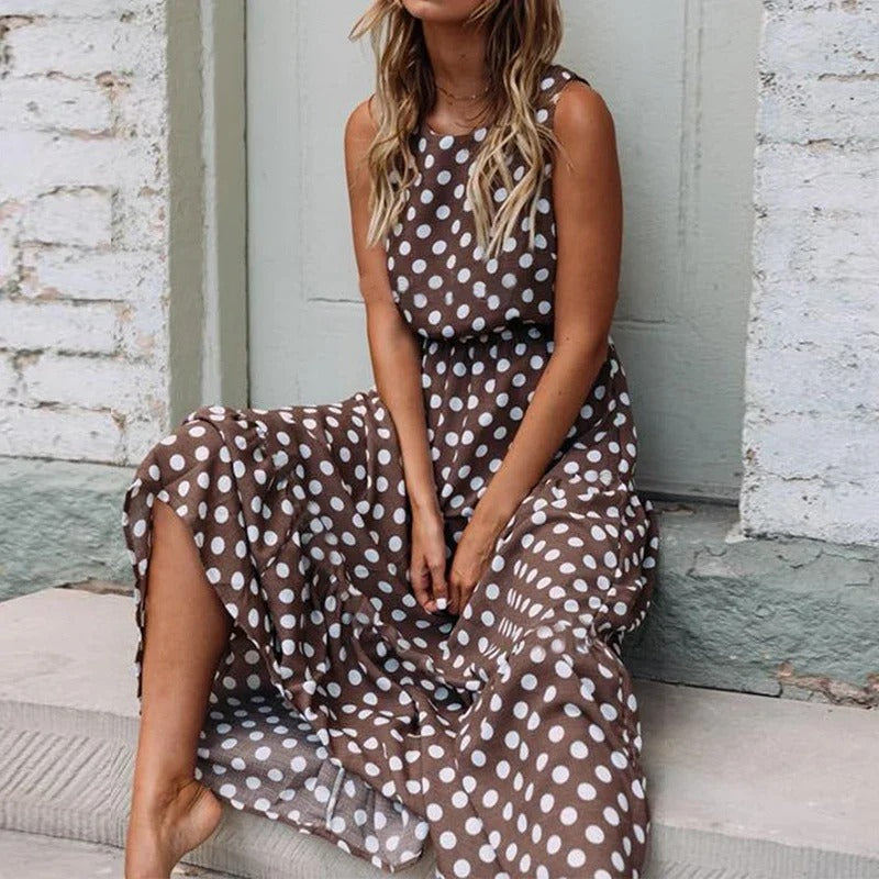 Woman sitting on a stone step in the brown polka dot dress, showing the gathered waist and tiered, flowing skirt. 2