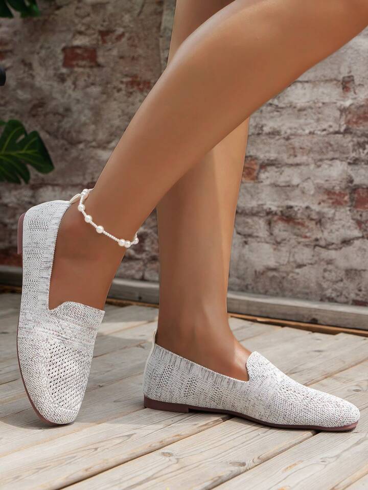 Light grey knit slip-on shoes worn with a pearl anklet, side view against a brick wall. 14