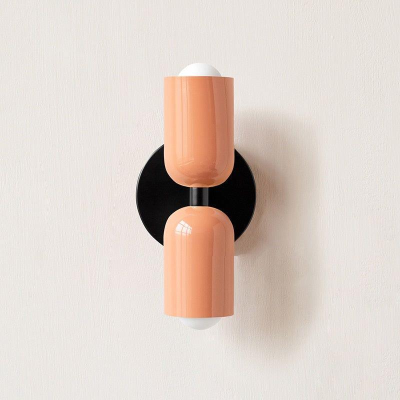 Wall light with two peach heads on a round black backplate, front view against a plain wall. 4