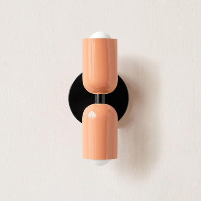 Wall light with two peach heads on a round black backplate, front view against a plain wall. 4