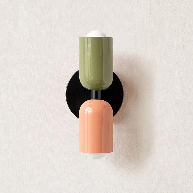 Wall light with a green upper head and peach lower head on a round black backplate, front view. 13