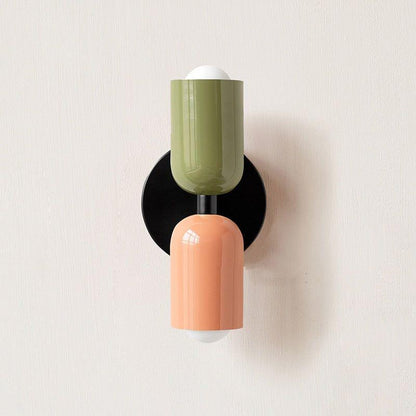 Wall light with a green upper head and peach lower head on a round black backplate, front view. 13