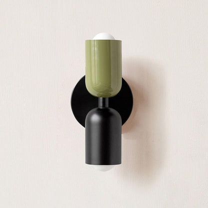 Wall light with a green upper head and matt black lower head on a round black backplate, front view. 12