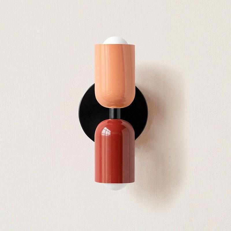 Wall light with a peach upper head and deep red lower head on a round black backplate, front view. 6