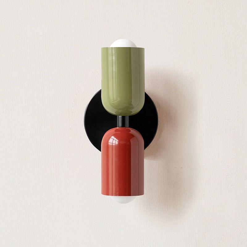 Wall light with a green upper head and red lower head on a round black backplate, front view. 11