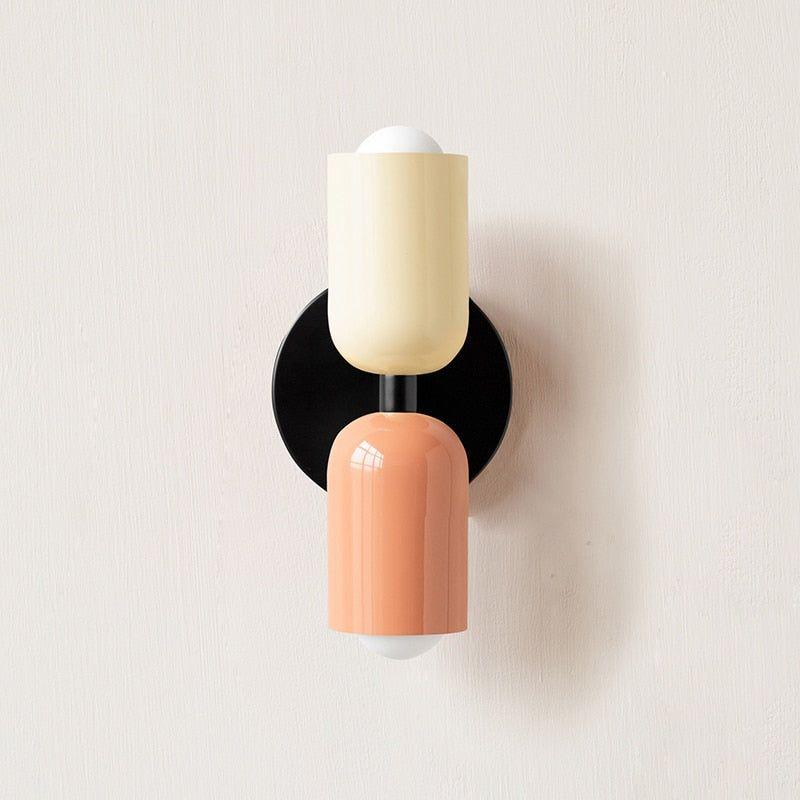 Wall light with a cream upper head and peach lower head on a round black backplate, front view. 3